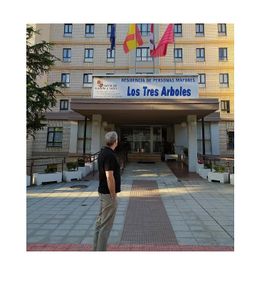 Una persona que observa un edificio. El edificio es de varios pisos y tiene una entrada principal con el nombre Residencia 'Los Tres Árboles'